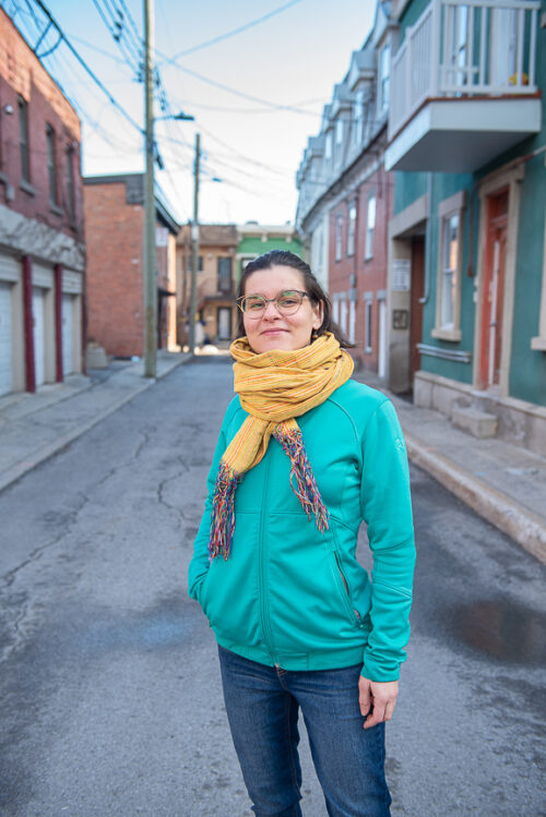 Femme souriante à la caméra avec une ruelle montréalaise en arrière plan.